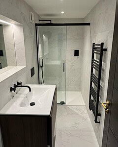 Angled view of a modern glass shower with towel rack, with a contemporary sink visible in the foreground.