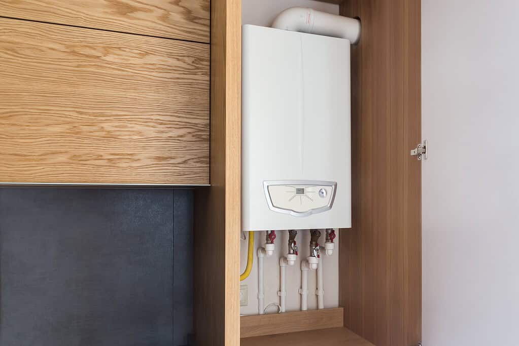 Domestic boiler installed inside a wooden cupboard for a tidy and space-saving home heating setup.