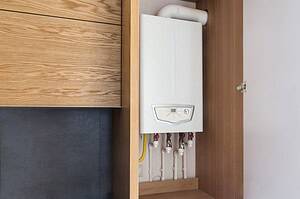 Domestic boiler installed inside a wooden cupboard for a tidy and space-saving home heating setup.